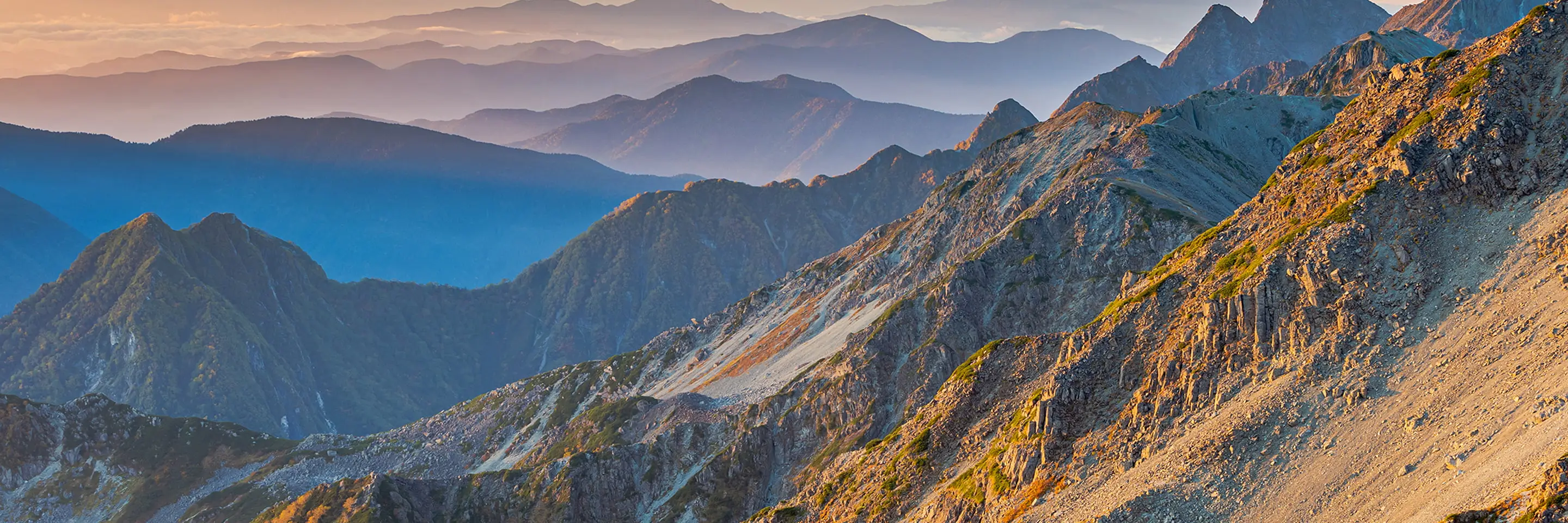 夕暮れ時の山脈を撮影した風景写真。重なり合う山々が霞んで層状に見える