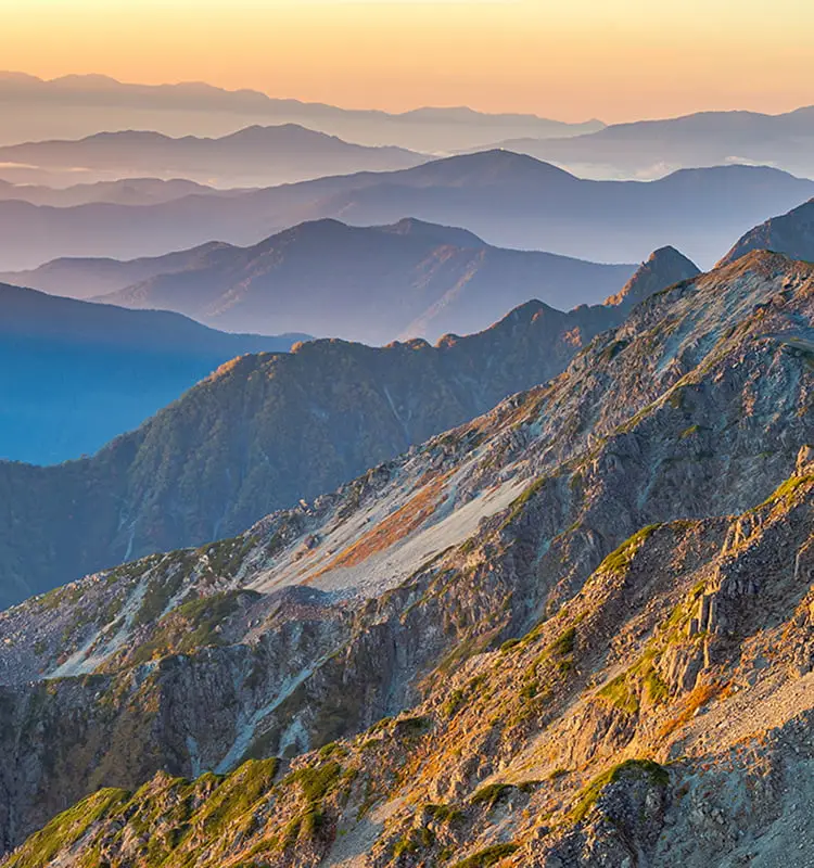 夕暮れ時の山脈を撮影した風景写真。重なり合う山々が霞んで層状に見える
